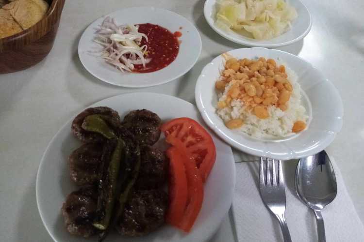 Grilled köfte with green pepper and tomato slices, rice with beans, smashed tomato sauce with onions, and sliced bread at BİRTAT Köfte Salonu in Edirne.
