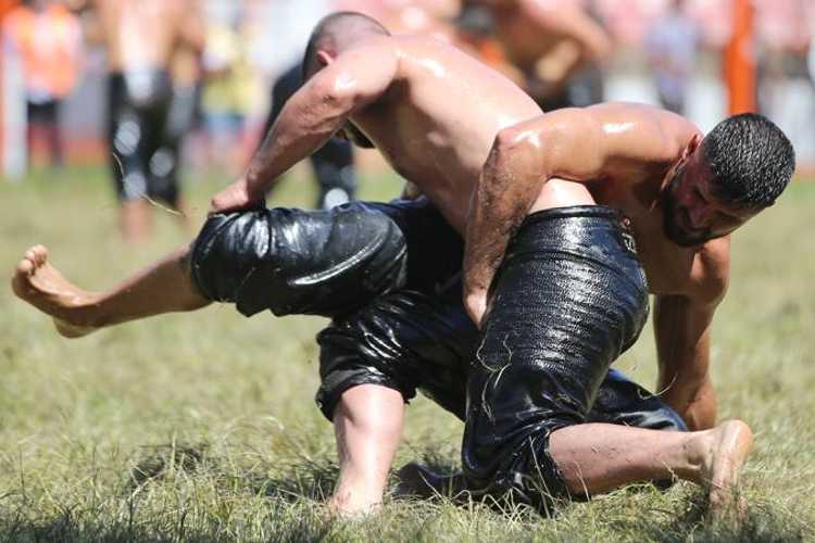 Traditional oil wrestling match with two athletes grappling on grass