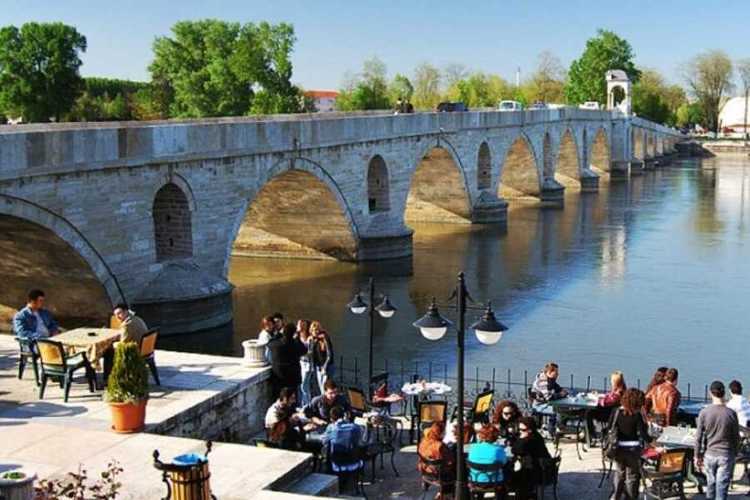 Meriç Bridge on the left with river flowing and a riverside café with people in Edirne