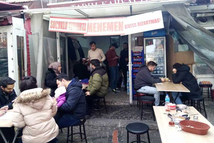 Entrance of Tadım Menemen in Kaleiçi with waiter serving outdoor tables and diners seated outside.