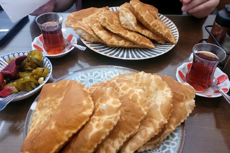 Traditional Eskişehir çiğbörek served with a glass of Turkish tea and pickles