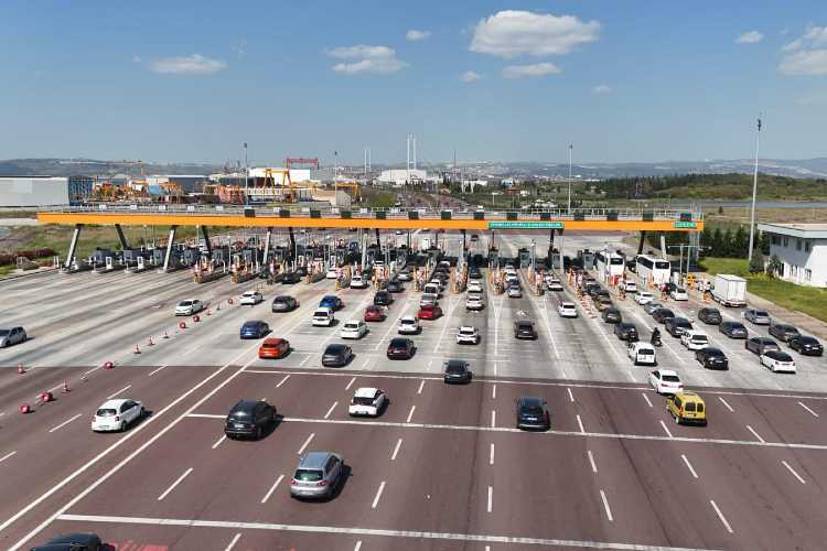 "Cars passing through a Turkish motorway toll plaza with HGS and OGS lanes, booths, and signage, on a sunny day with scenic hills in the background."