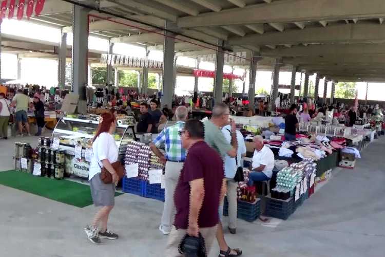 Inside Edirne Saturday Market (Cumartesi Pazarı) showing crowded indoor-style aisles with shoppers browsing fresh produce, textiles, and local goods under canopy-covered stalls.