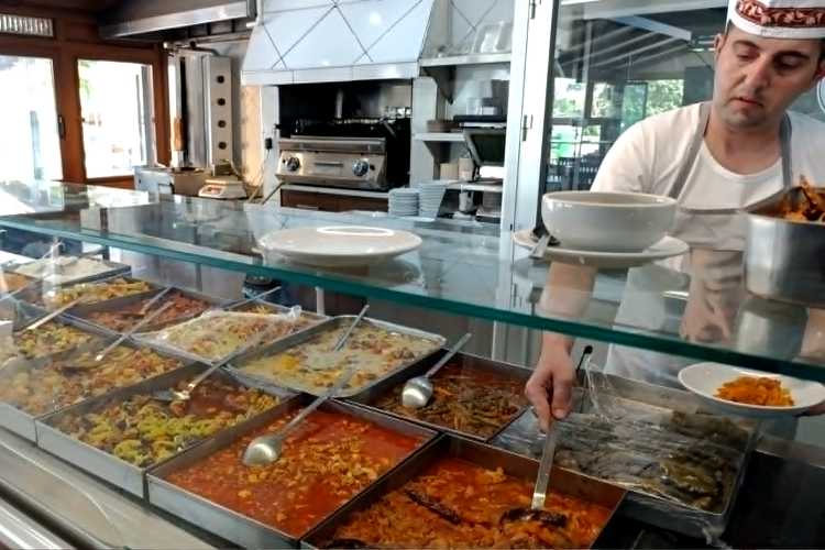 Chef serving food at the hot food counter in Ustam Restaurant Edirne with various traditional dishes